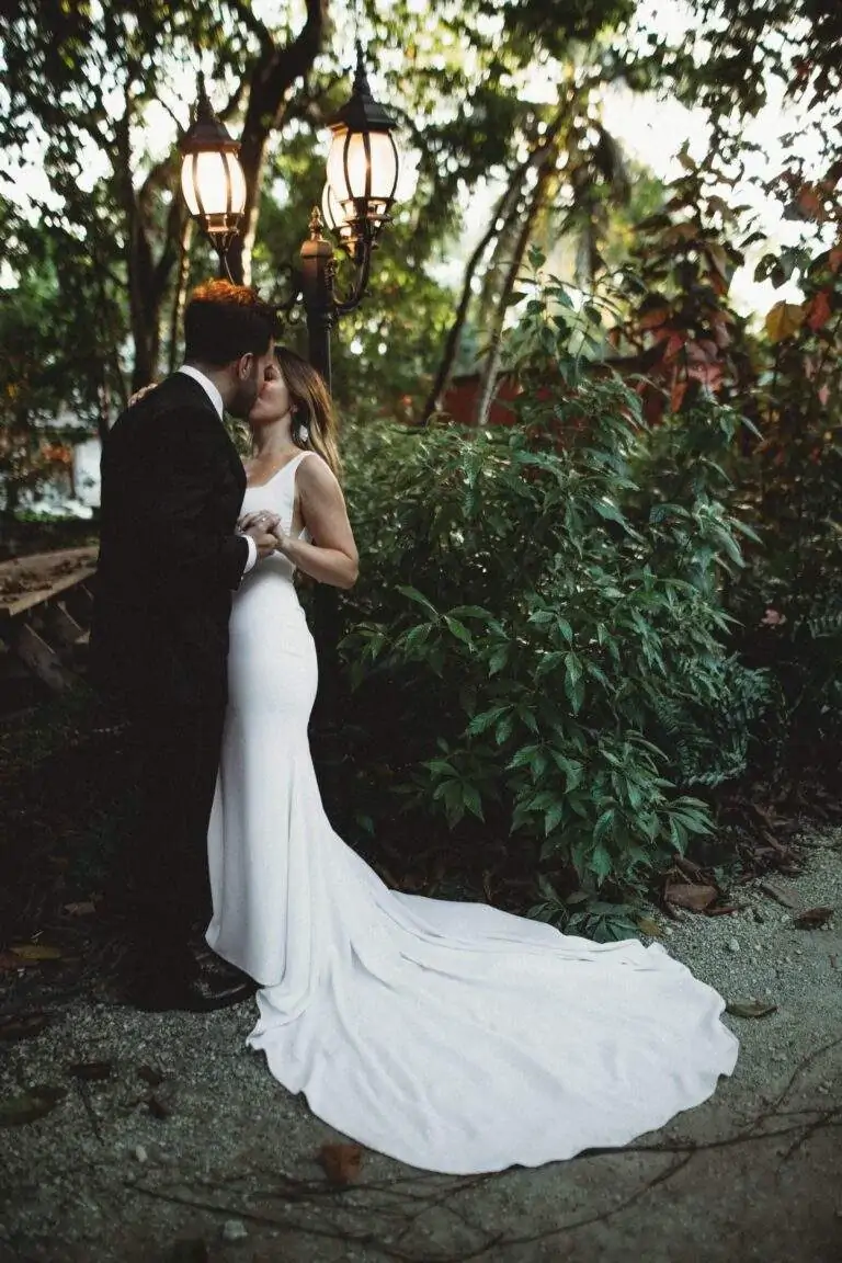 A bride and groom stand closely holding hands as they pose for a photo.