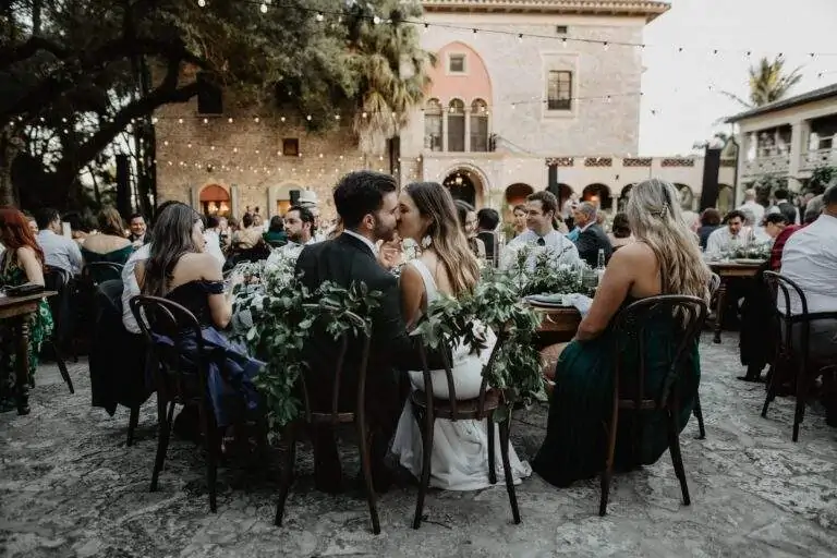 A bride and groom share a kiss as they sit at their wedding reception.