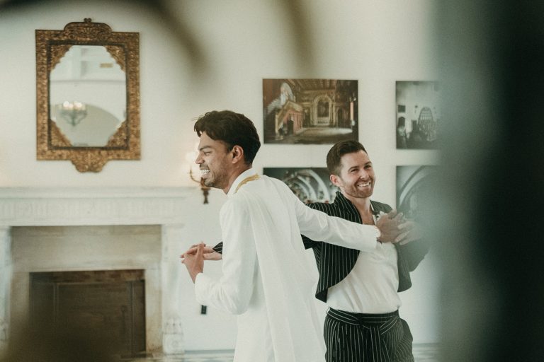 Grooms laughing while posing inside Deering Estate's historic Stone House Museum's grand hall ballroom