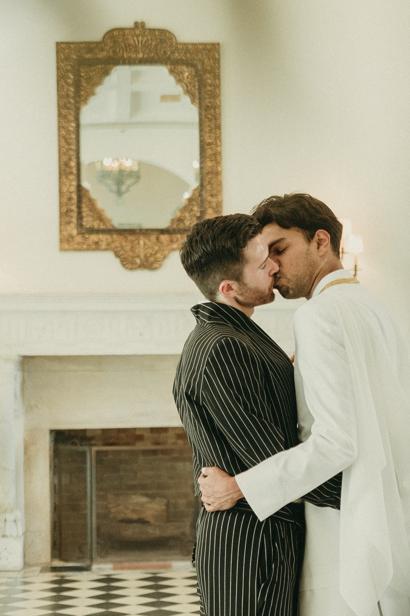 Grooms embracing inside Deering Estate's historic Stone House Museum's grand hall ballroom. The Grand Hall Ballroom's fireplace is in the background.