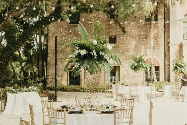 Detail photo of a reception table in Deering Estate's historic Courtyard with delicate bistro-string lights above the table and the Stone House Museum in the background