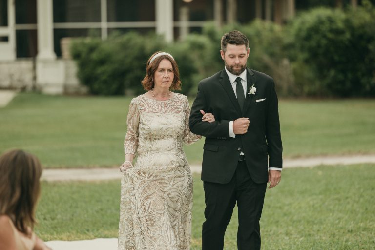 Two members of the wedding party, one woman and one man, walking down the aisle with the historic Richmond Cottage museum in the background