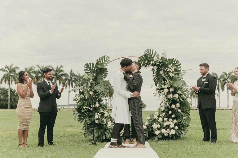 Grooms embracing each other at the end of their ceremony while the four members of their wedding party are standing on either site of them clapping