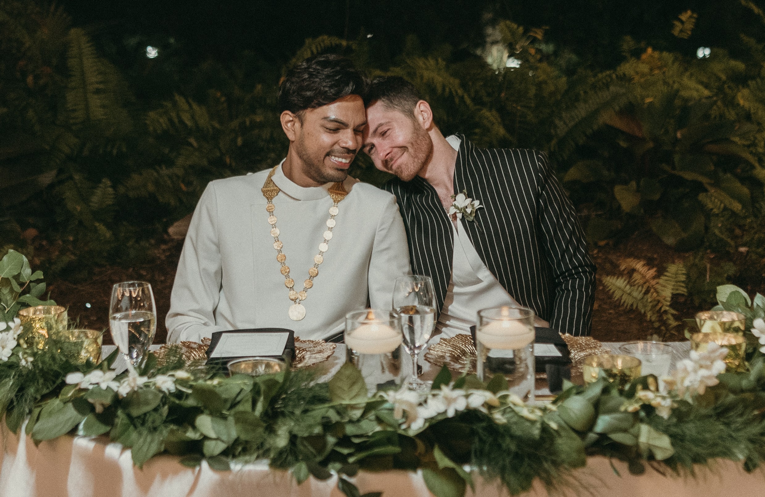 Grooms seated at their sweetheart's table laughing and embracing during a wedding speech