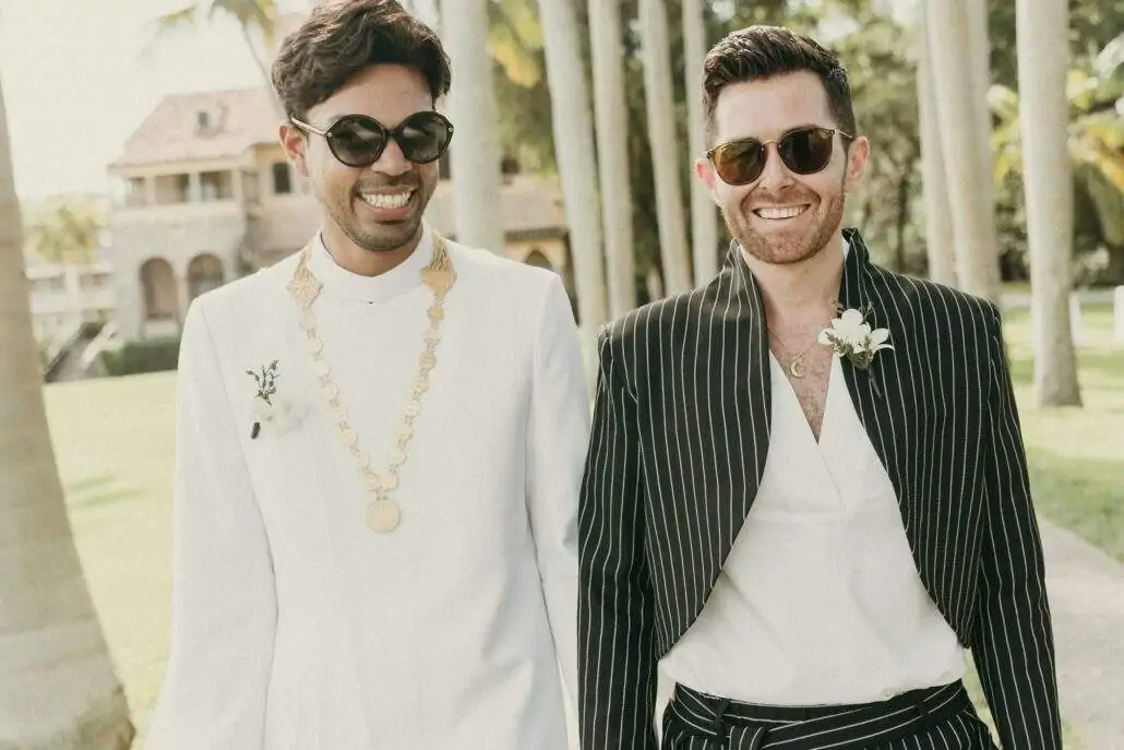 Photo of both grooms, Ismail (left) and Stephen (right) walking down Deering's Royal Palm Grove with the Stone House Museum in the background.