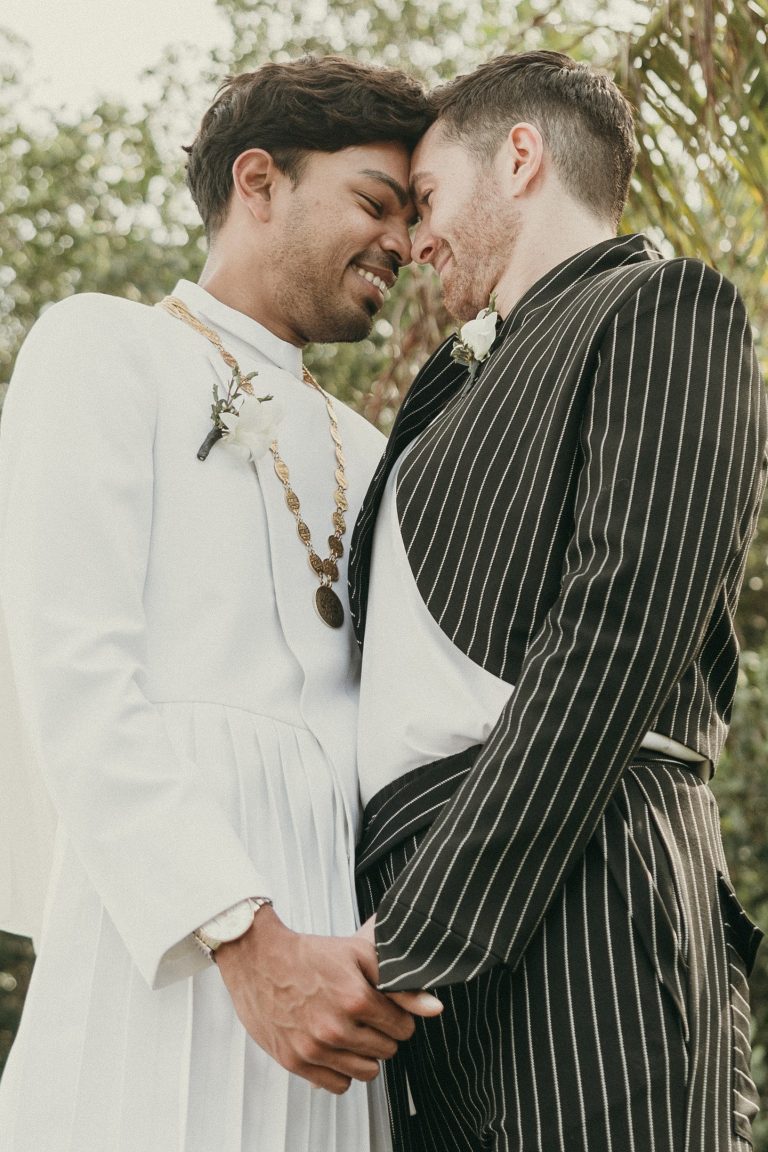 Grooms embracing each other with Deering Estate's natural gardens in the background