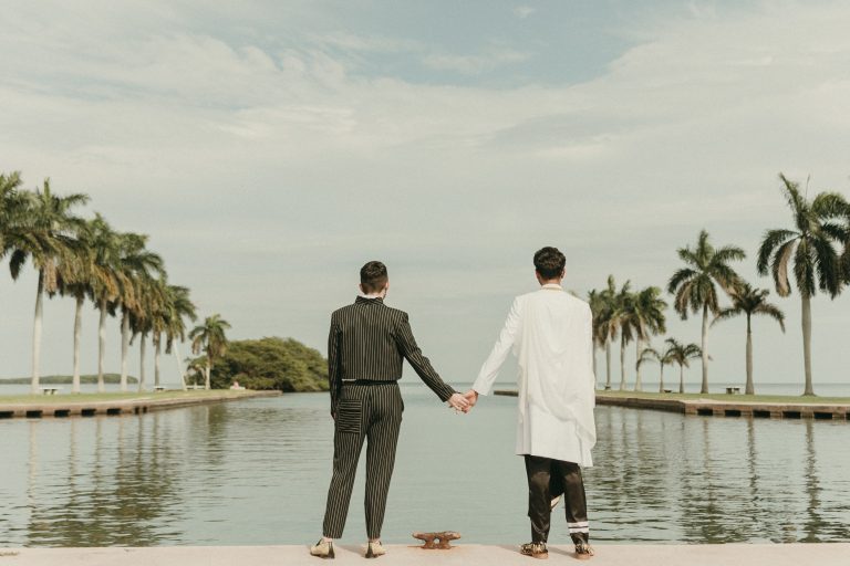 Grooms at Deering Estate's waterfront boat basin looking away from the camera towards Biscayne Bay while holding hands