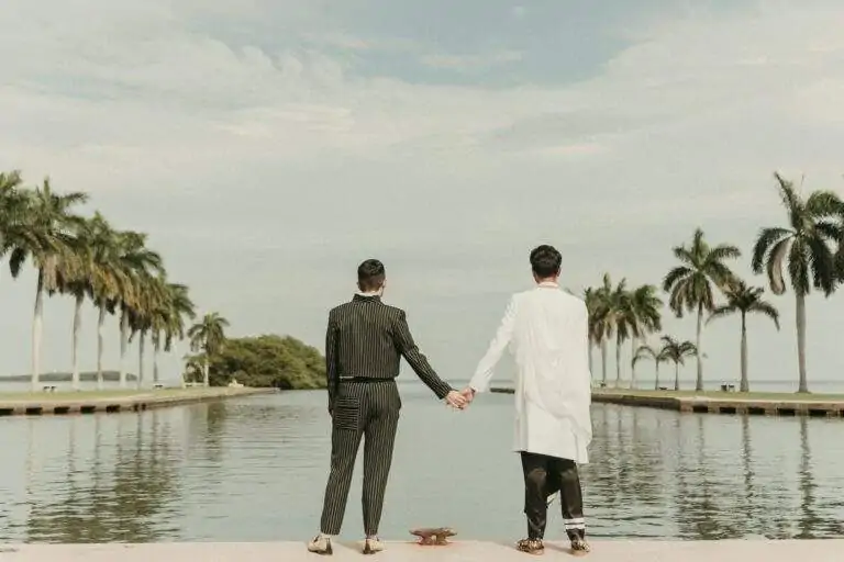 Grooms at Deering Estate's waterfront boat basin looking away from the camera towards Biscayne Bay while holding hands
