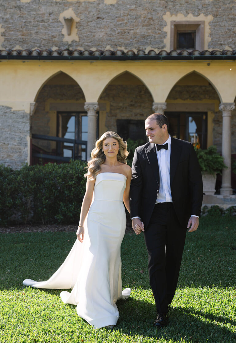 A bride and groom walk away from the Stone House hand-in-hand. As the bride looks off to the side, the groom is looking lovingly at the bride.
