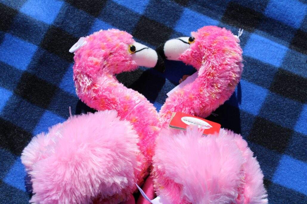 Two flamingo plushies facing each other so that their heads and necks make the shape of a heart.