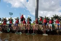 Eleven kids with red life vests on sitting with nets ready to catch critters.